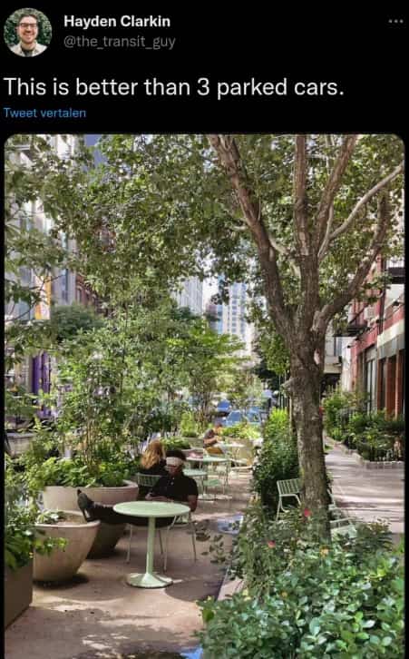 Pedestrian outdoor seating area with green plants replacing parking spaces on city street.