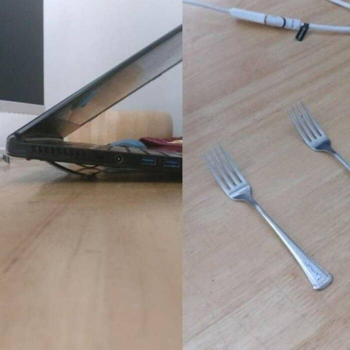 Two metal forks placed under a laptop to prevent it from overheating.