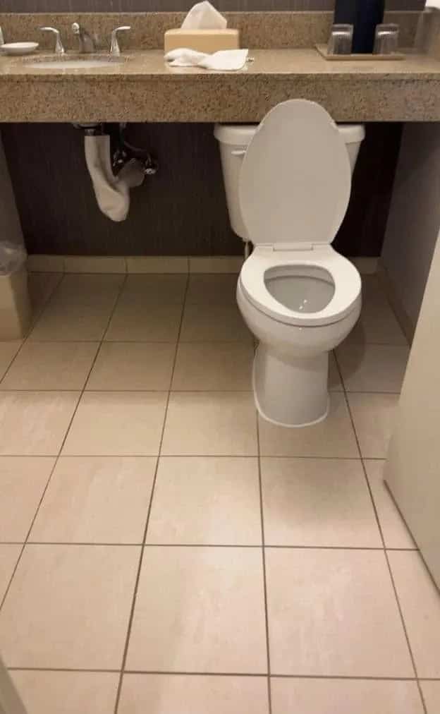 A toilet awkwardly installed beneath a low vanity countertop demonstrating a terrible bathroom design layout.