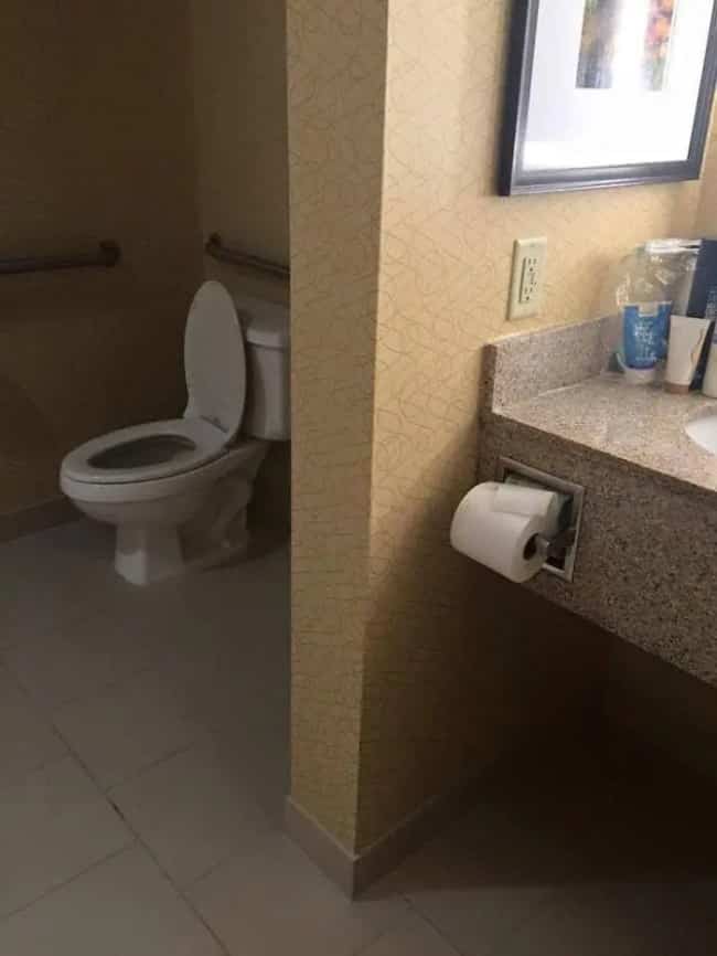 Toilet paper roll mounted on a sink wall unreachable from the adjacent toilet stall partition.