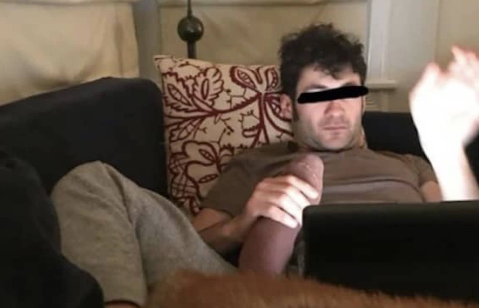 Man sitting on couch creating optical illusion holding feet to look like an explicit adult scene.