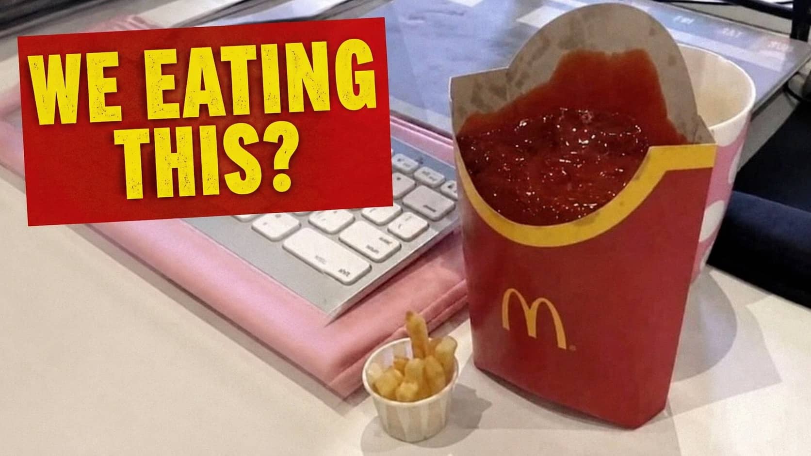 Large McDonald's French fry carton filled completely to top with ketchup next to laptop.