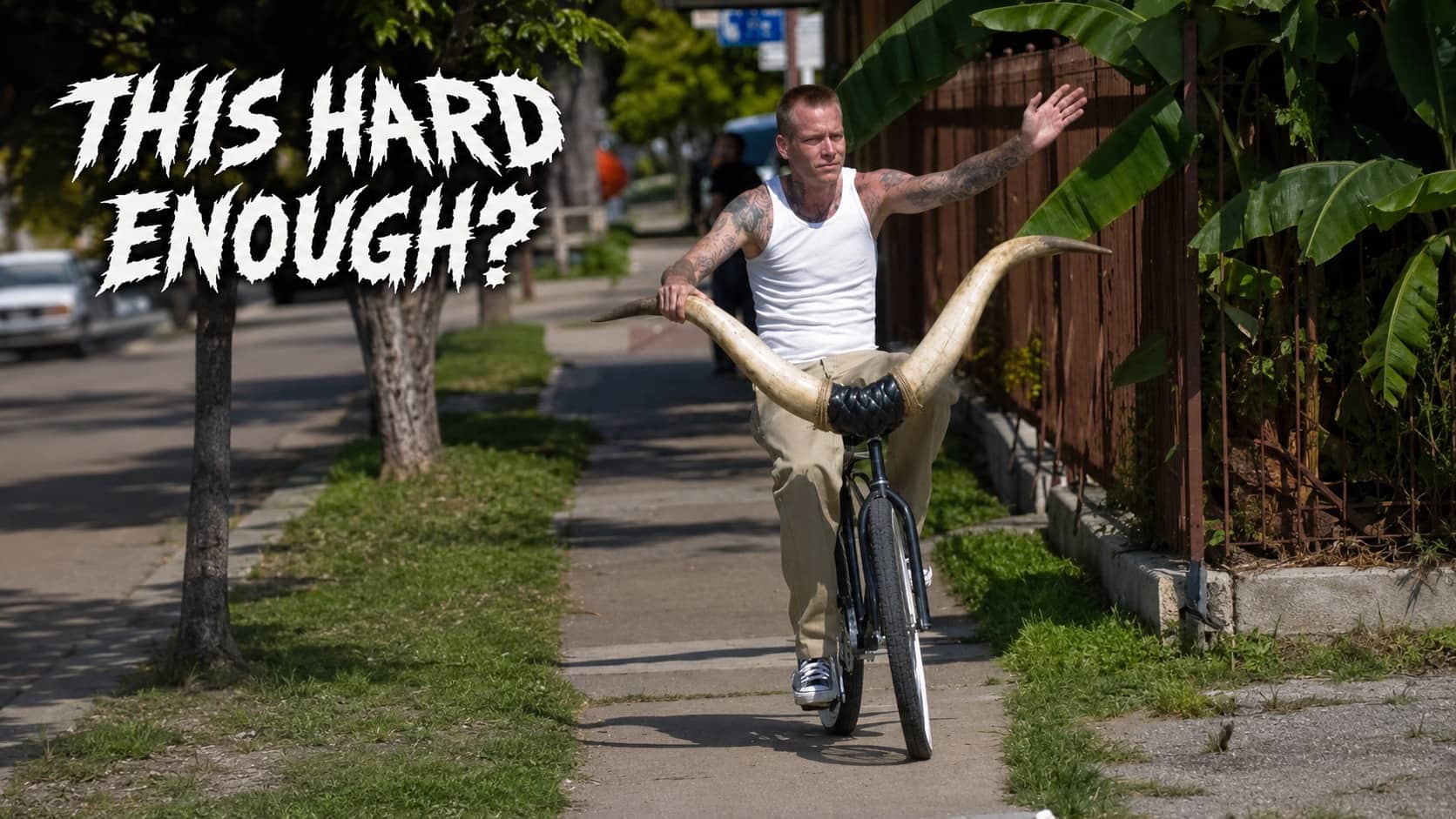 Tattooed man riding bicycle with large steer horns with text this hard enough