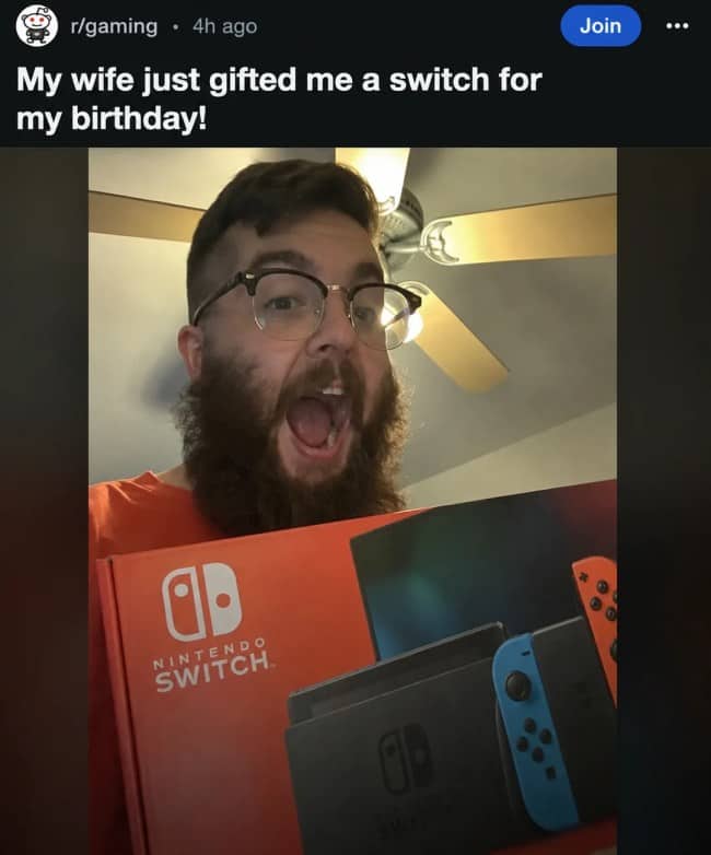 Excited bearded man proudly holding up a brand new Nintendo Switch gifted by his wife.
