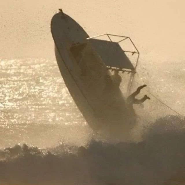 Motorboat airborne launching vertically high above rough ocean waves near shoreline.