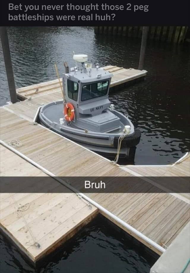 Tiny miniature navy boat docked alongside wooden pier looking surprisingly small.