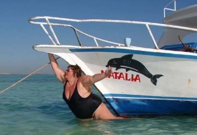 Woman posing dramatically underwater hanging onto the bow of a boat.