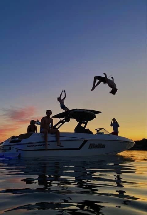 Group of friends hanging on speedboat with guy performing high backflip off roof.