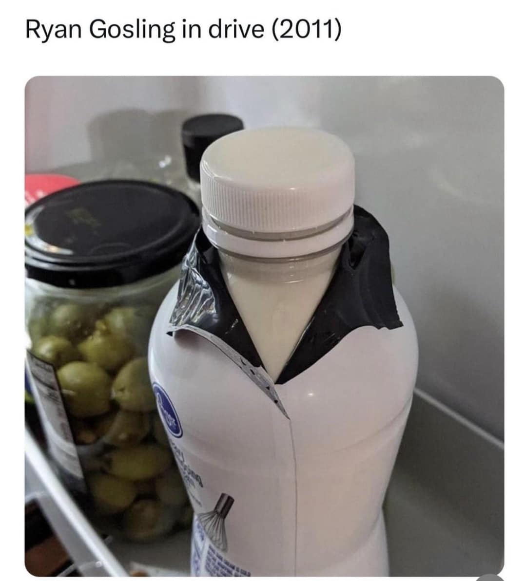 salad dressing bottle inside a refrigerator with its black plastic shrink-wrap peeled down into a sharp V-neck collar, forming a classic meme parody of Ryan Gosling's jacket in Drive.