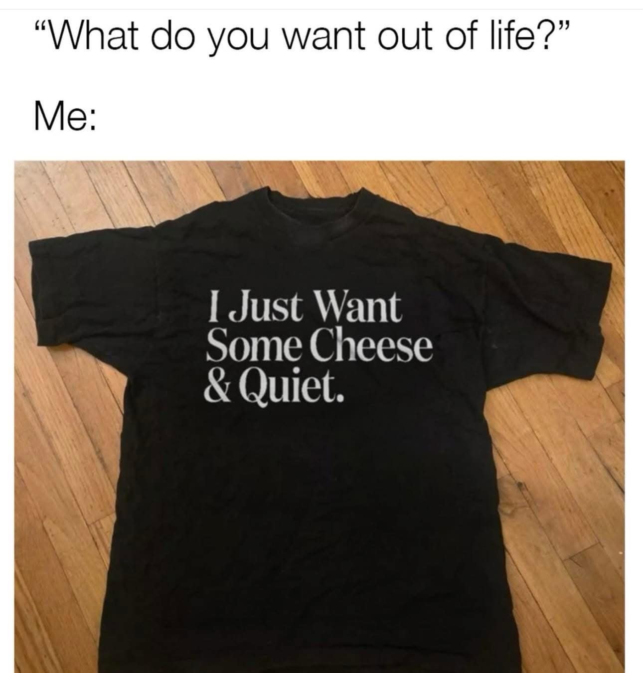Flat-lay photo of a plain black t-shirt printed with white text reading "I Just Want Some Cheese & Quiet" as a life goal response.
