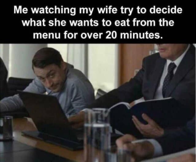 Kieran Culkin playing Roman Roy in Succession, peering over a laptop with an impatient expression during a boardroom scene.