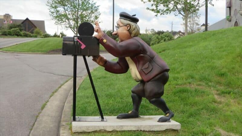 Vintage photographer statue taking photos with a camera shaped into a cool mailbox on a lawn.