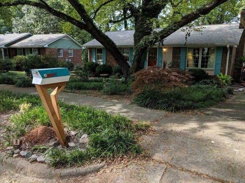 Mid-century modern teal cool mailbox with a stylish angled wooden post in a manicured yard.