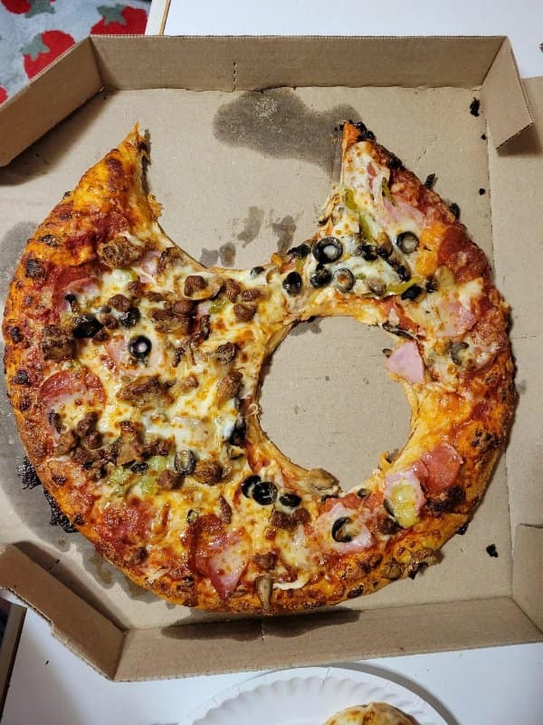 A pepperoni and black olive pizza inside a delivery box where someone ate out the entire middle circle, leaving an empty ring of outer crust.