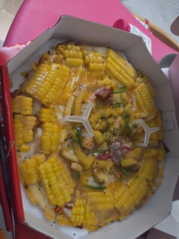 Specialty delivery pizza heavily topped with full cross-section chunks of corn on the cob alongside french fries and melted cheese.