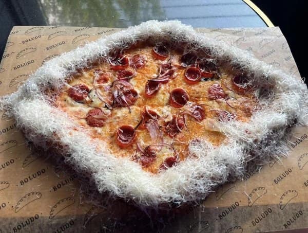 Pepperoni and red onion pizza surrounded by an extraordinarily thick, furry border ring of finely shaved parmesan cheese along the outer crust.