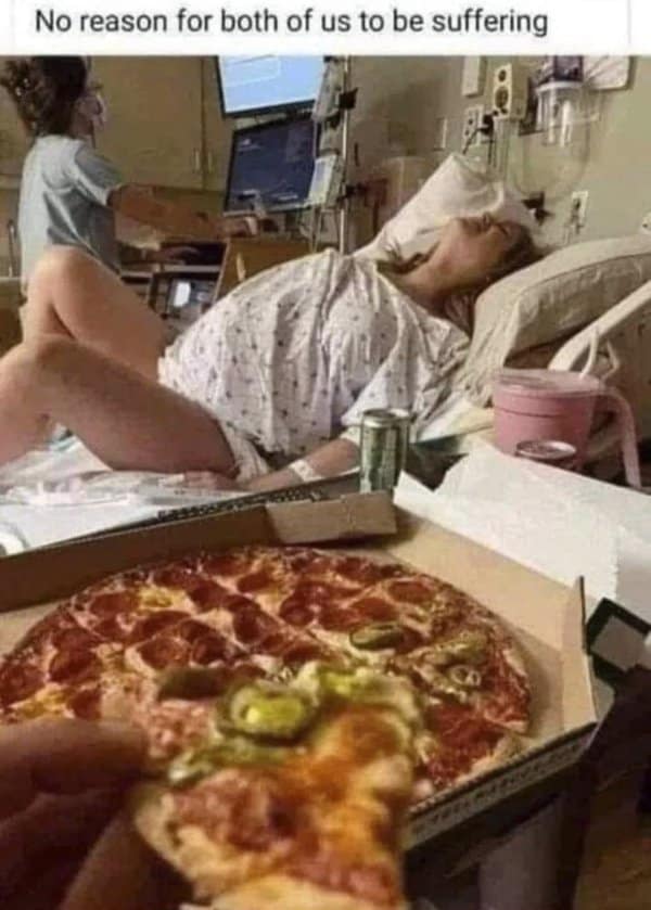 A person holding a fresh slice of pepperoni jalapeño pizza in a hospital room while a woman endures active labor in the bed behind them.