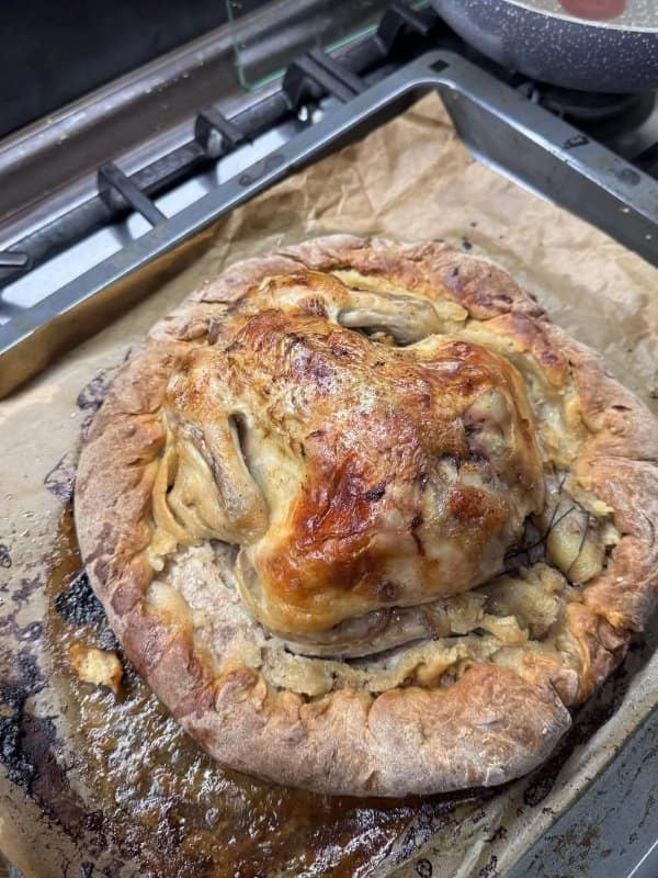 An entire whole-roasted chicken baked directly into the center of a thick dough crust on a parchment-lined sheet pan.