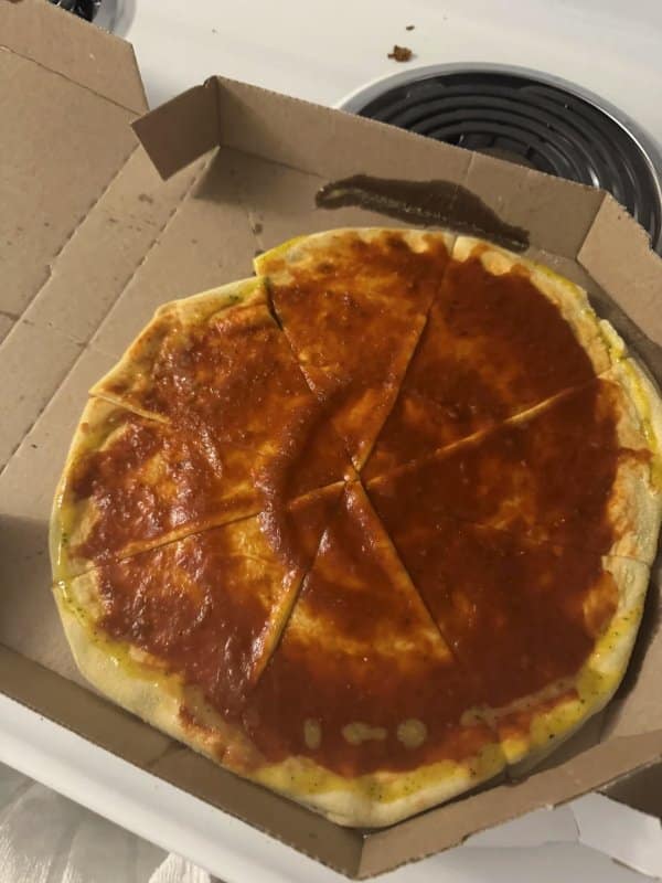 Cursed pizza delivery box containing a pale, underbaked dough round slathered only in watery red tomato sauce without a single strand of cheese.