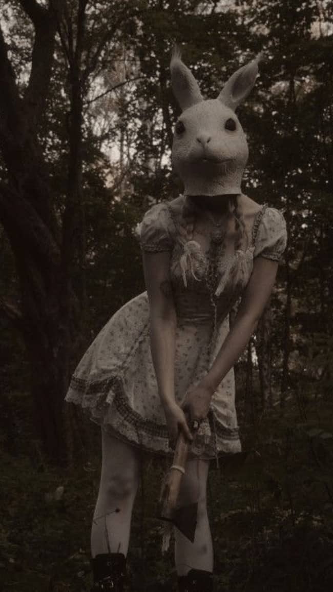 Person wearing a creepy rabbit mask holding an axe in the woods looking cute but terrifying.