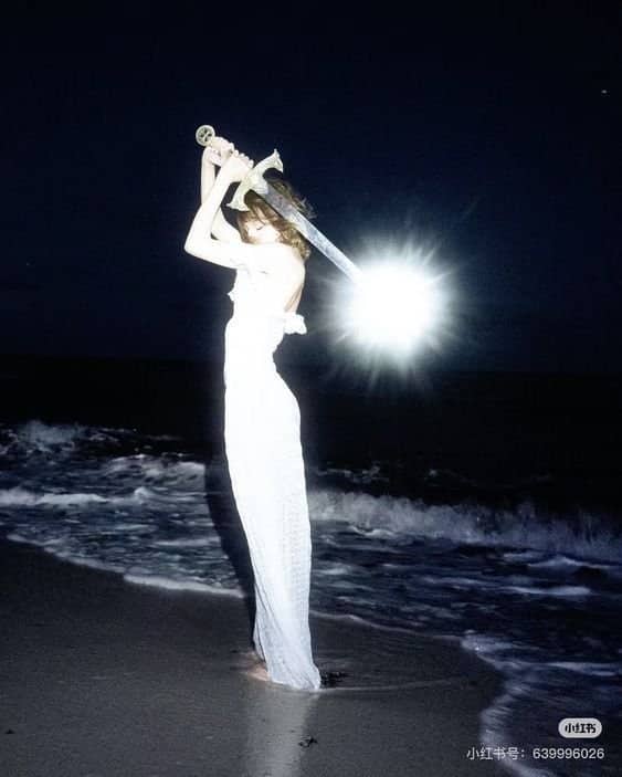 Woman wielding a brightly glowing sword on a dark beach looking cute but terrifying.