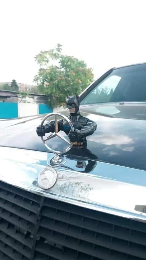 Creative hood ornament featuring Batman action figure holding onto a Mercedes-Benz car logo emblem.