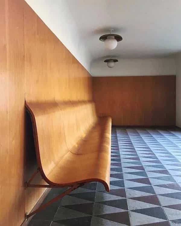 Curved wooden bench attached to wall along hallway with patterned tile floor funny memes.
