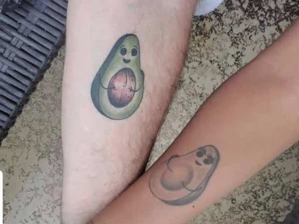 Two arms displaying matching avocado tattoos with one holding the pit inside funny memes.