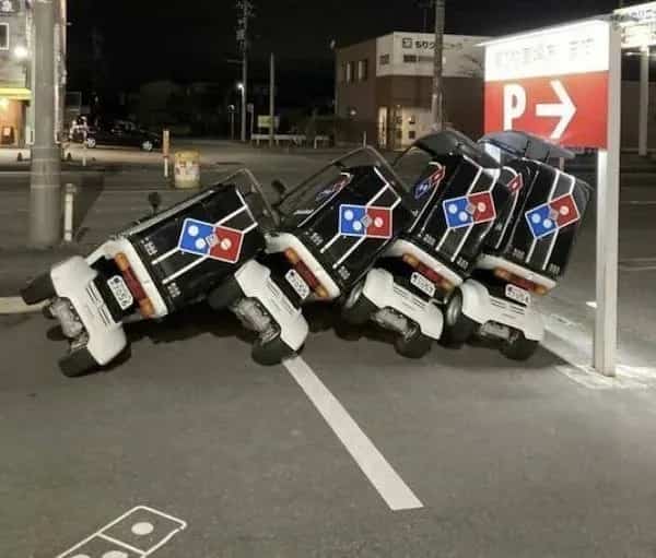 Domino's delivery scooters tipped over in a line like dominoes in a parking lot.