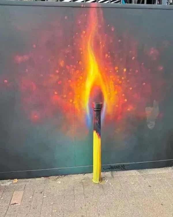 Street bollard painted to resemble a matchstick burning with colorful spray paint flame memes