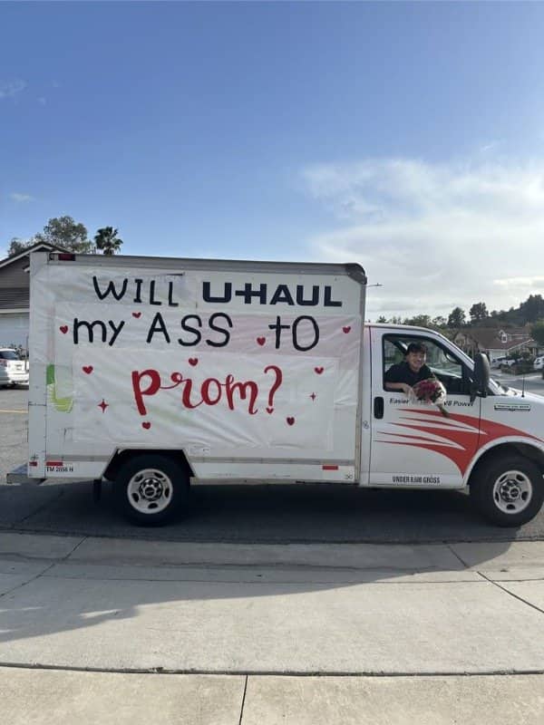 Boy driving a U-Haul truck with a banner asking someone to prom.