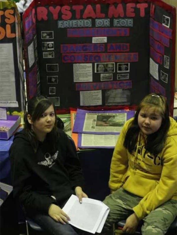 Two middle school girls sitting sullenly in front of a Crystal Meth science project.