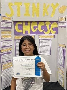 Girl holding a first place certificate in front of her Stinky Cheese project.