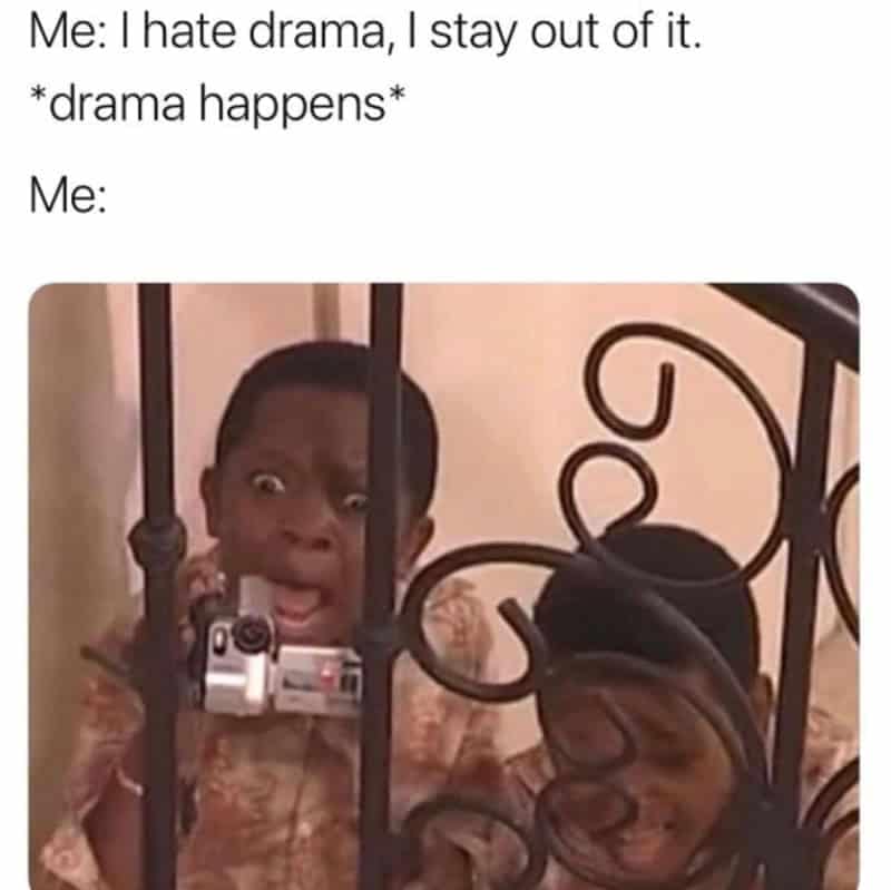 A young kid presses wide, excited eyes against stair banister bars while filming with a handheld camcorder, perfectly portraying someone secretly loving the drama they claim to avoid in a funny introvert meme.
