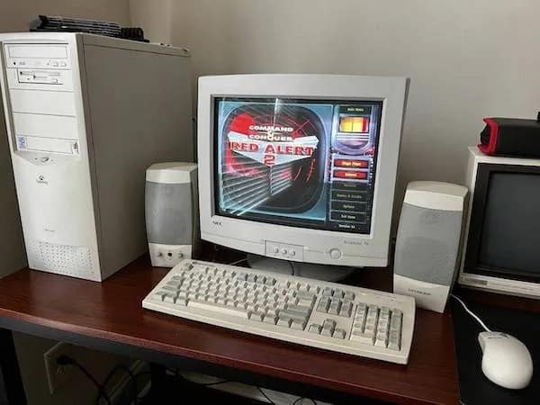 A retro gaming meme dump photo of a classic 2000s beige desktop computer setup featuring a bulky CRT monitor displaying the main menu of Command & Conquer: Red Alert 2.