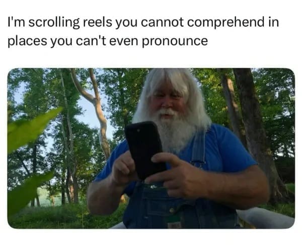 An outdoor elder scrolling post operating as a hilarious meme showing a bearded man in overalls in the woods holding a smartphone under text about scrolling reels in unpronounceable places.