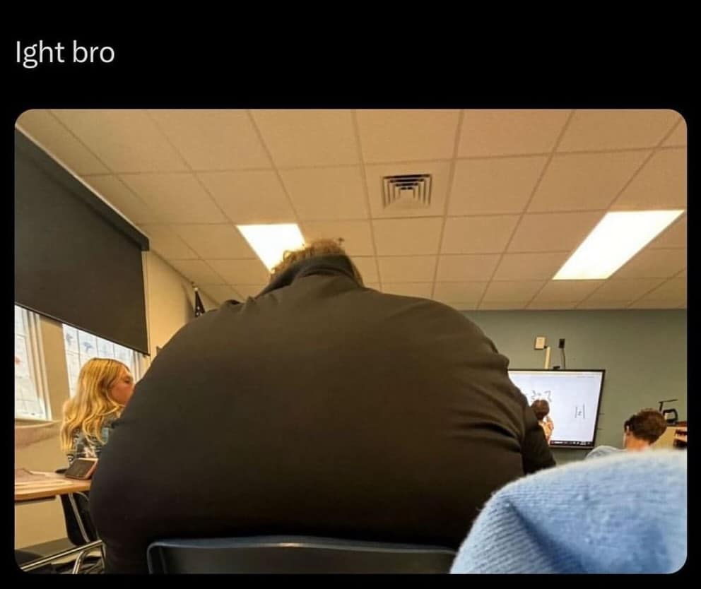 A view from behind a student whose massive back and shoulders completely block the front whiteboard, captioned "ight bro."