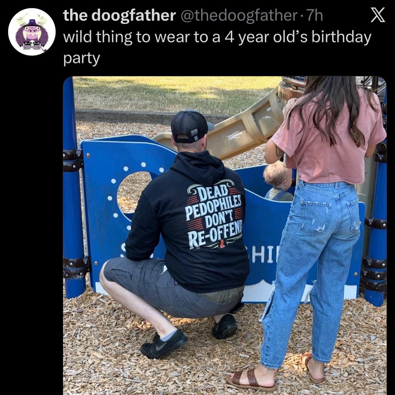 Spotted at a children's playground, a man crouches near a plastic slide wearing a heavy black hoodie printed with "DEAD PEDOPHILES DON'T RE-OFFEND" in an awkward public meme dump photo.