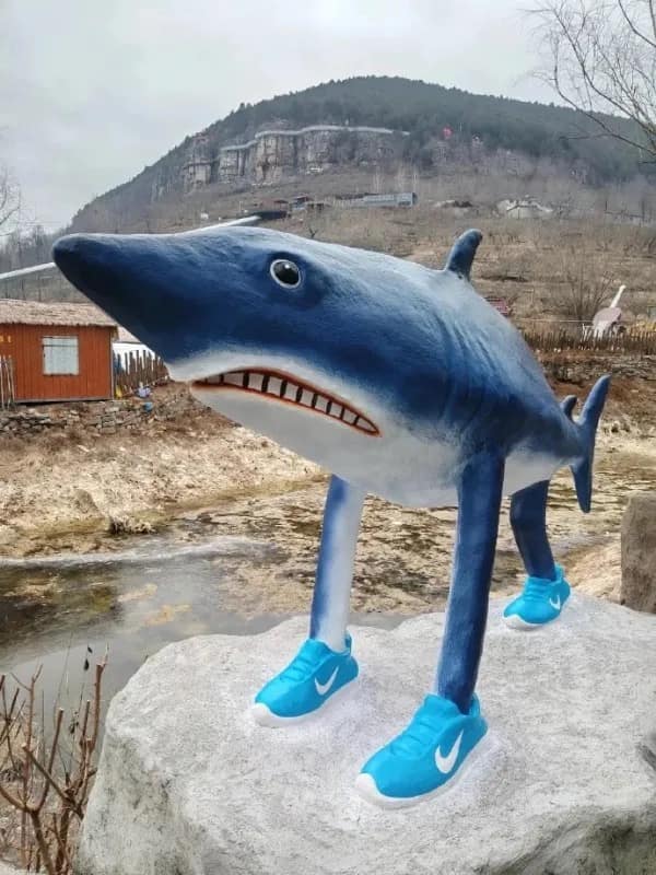 A bizarre roadside sculpture meme dump photo depicting a fiberglass blue shark standing upright on four long mammalian legs wearing bright blue Nike sneakers.