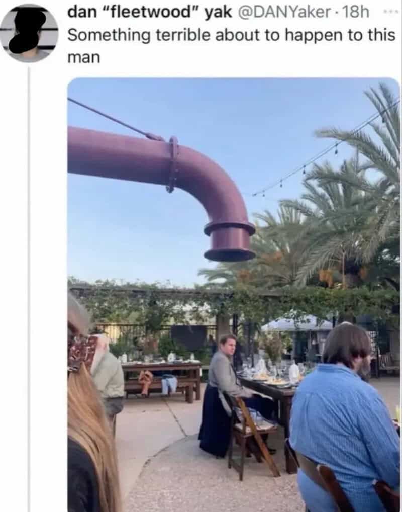 A giant industrial pipe hanging ominously directly above a man sitting at an outdoor patio dining table, paired with a funny tweet prediction in a meme dump.