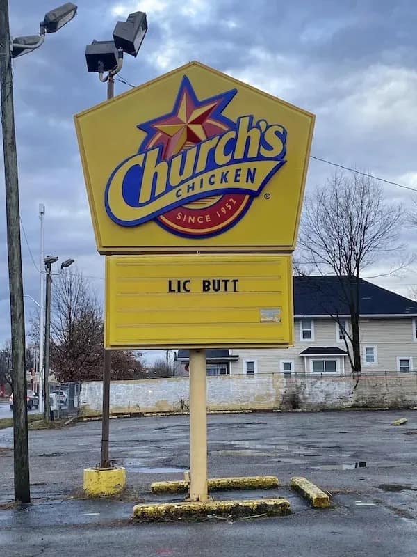 Roadside marquee sign for Church's Chicken where missing letters leave behind an accidental message reading "LIC BUTT".