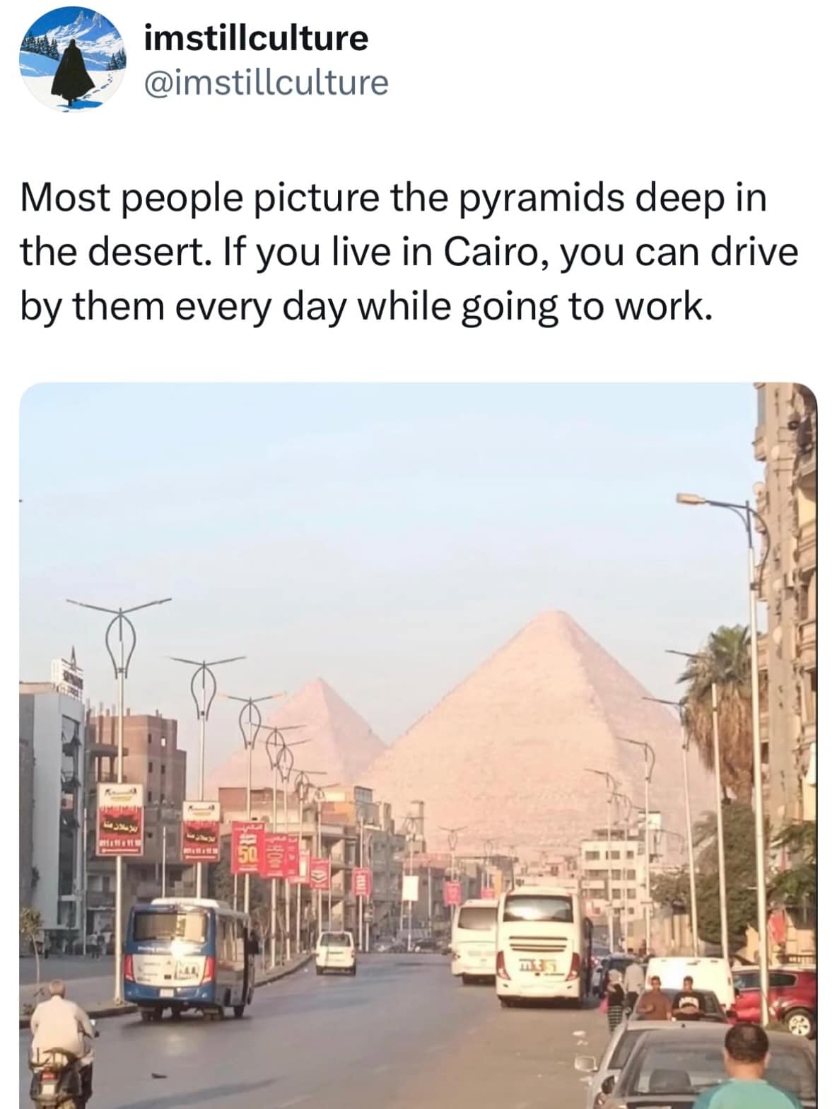 Cairo city traffic shot showing modern buses and streetlights framed directly in front of the colossal ancient Pyramids of Giza looming over urban apartments.