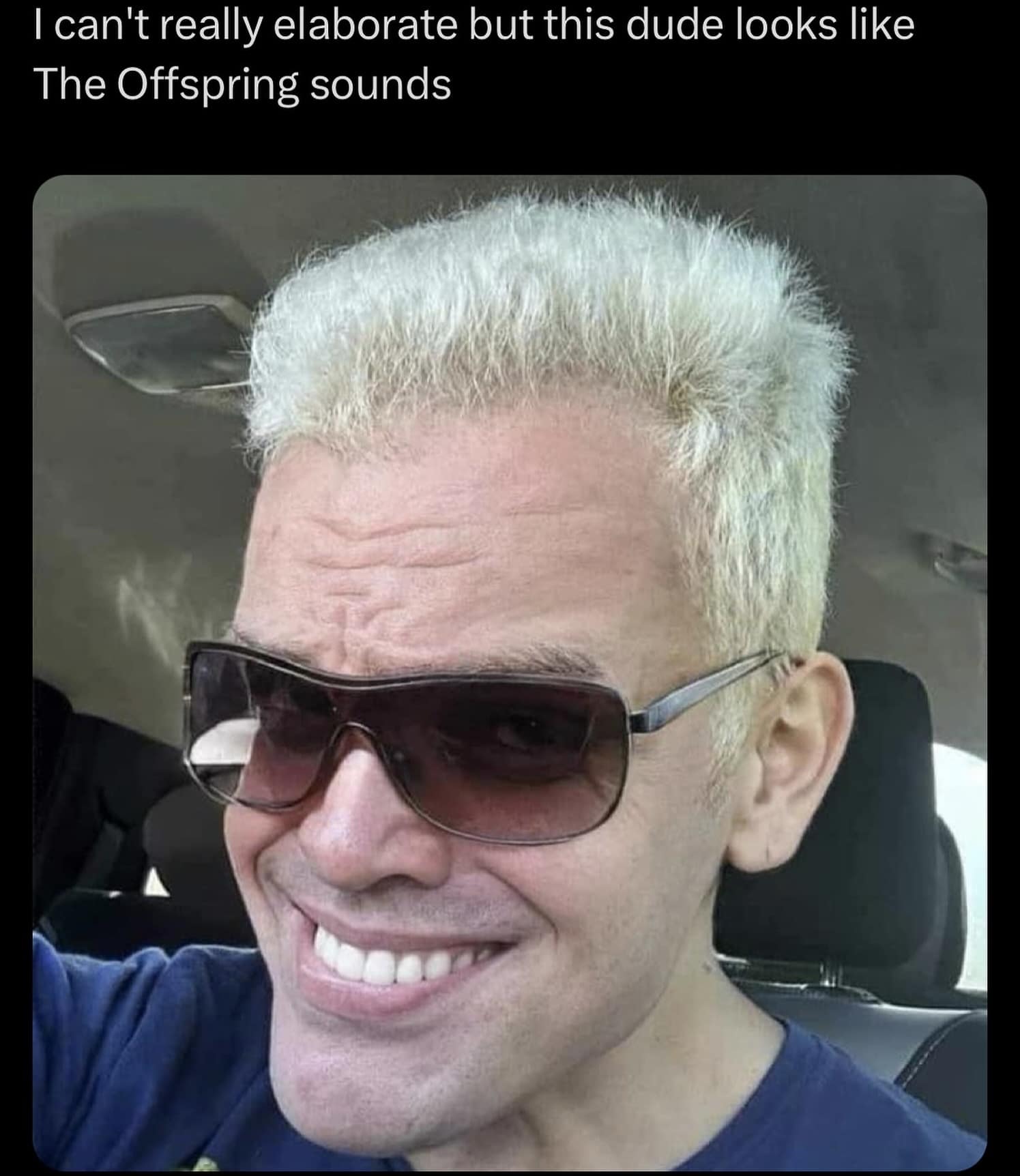 A man with spiked frosted-blonde hair and tinted sunglasses smirking in a car selfie, captioned as looking like 90s punk band The Offspring sounds.