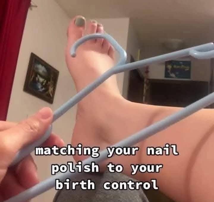A person holding a plastic coat hanger next to their foot to match their light-blue pedicure polish with the shape of an IUD.