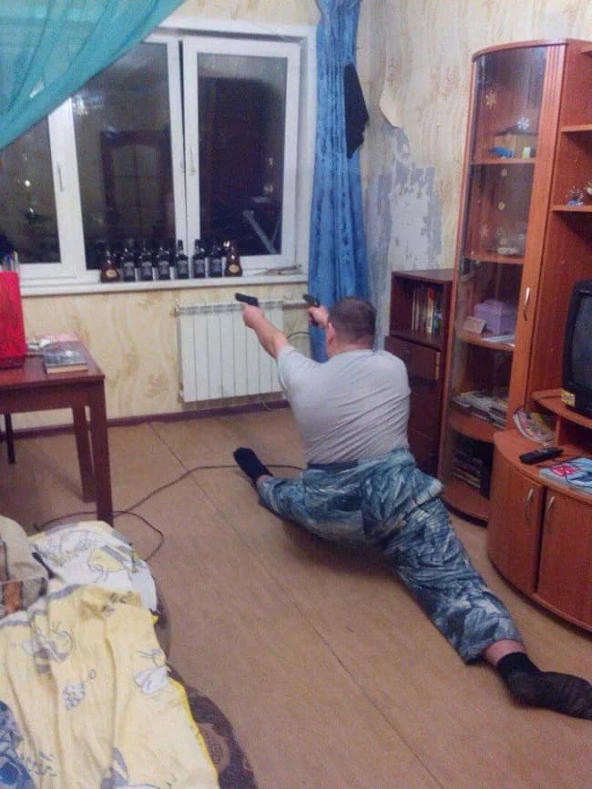 A chaotic tactical posture photo featured in this meme dump showing a man doing a full gymnastics leg split on his living room floor while aiming two handguns at a window.