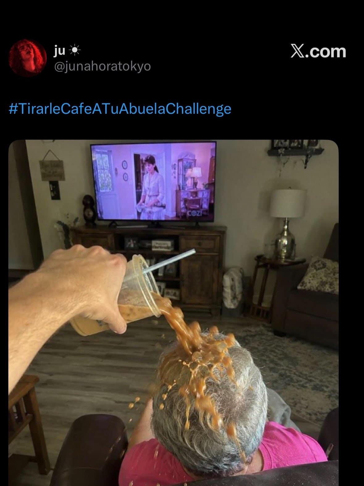 First-person view of someone pouring iced coffee directly onto an elderly woman's head while she watches television, tagged with an unhinged Spanish challenge hashtag.