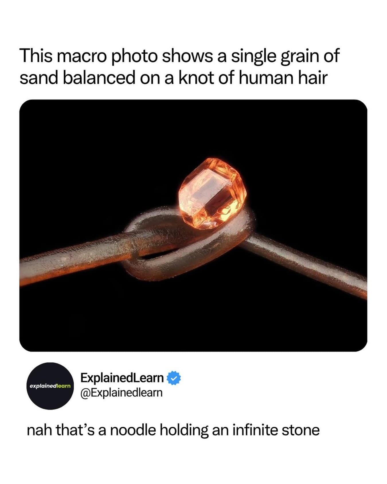High-magnification macro photograph showing a single orange grain of sand sitting on a knotted strand of human hair, jokingly compared to an Infinity Stone.