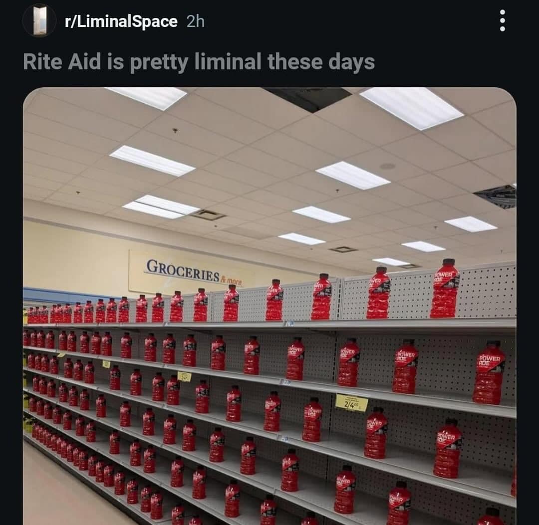 An eerie, sparsely stocked Rite Aid pharmacy aisle filled only with widely spaced red Powerade bottles on empty metal shelving.