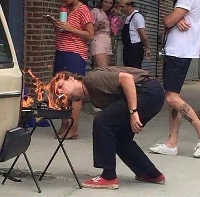 Wild viral meme of a guy lighting his cigarette directly off an open charcoal grill flame.