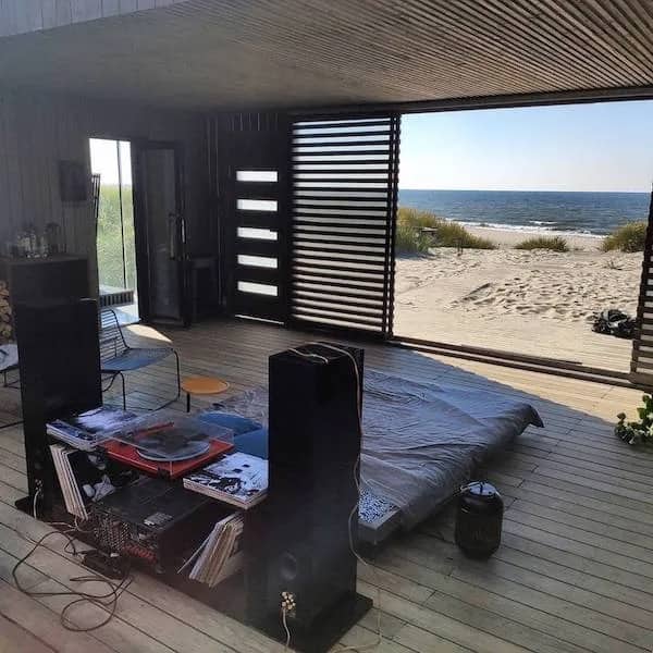 Cozy room with mattress on wooden deck opening directly to ocean beach shore view.